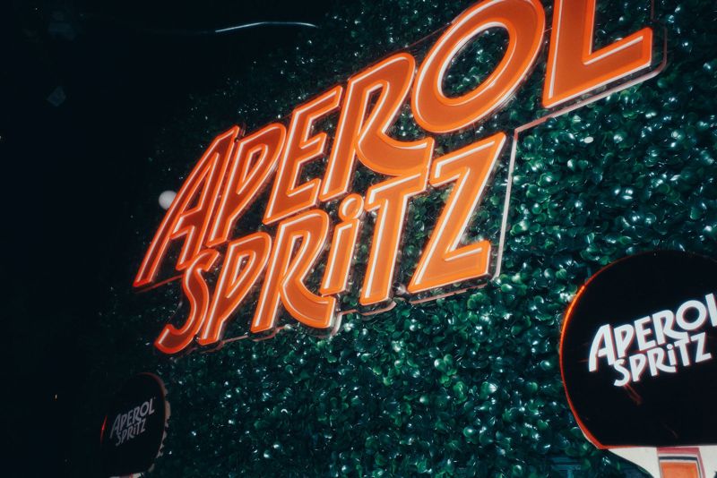 Aperol Spritz neon sign on a green hedge wall