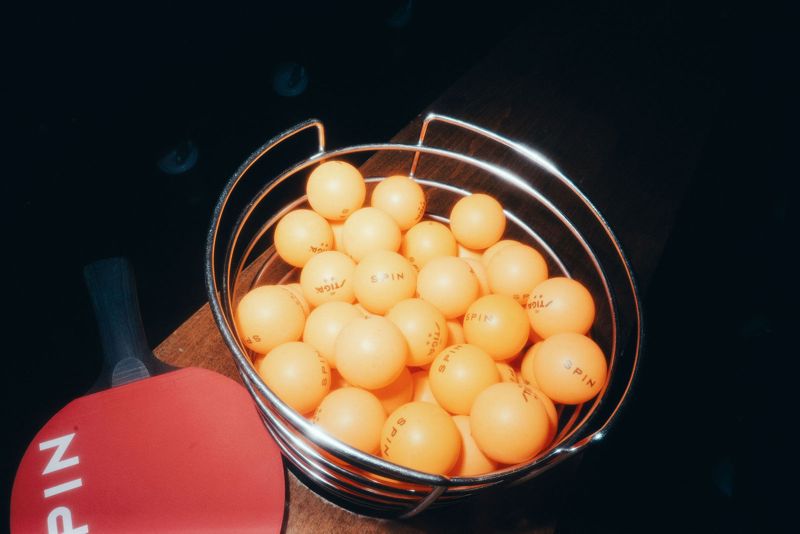 Basket of orange ping pong balls beside a Spin paddle